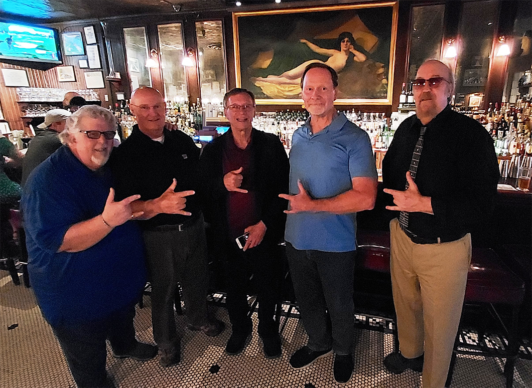 Members of Sutton Ho standing in a bar all making their band hand symbol
