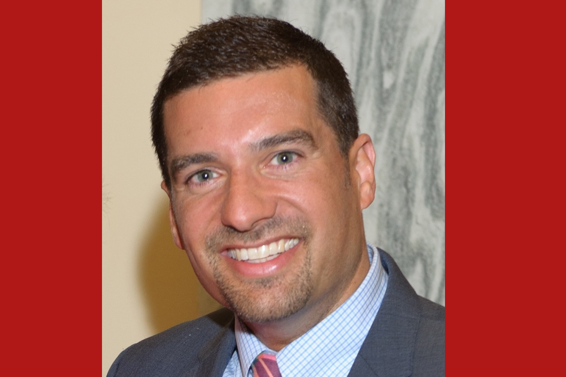 Image of Justin Burkhardt headshot, wearing blue suit with pink tie.